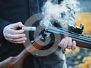 Smoke from the trunks of smooth-bore hunting rifle after firing. Hunter in camouflage takes out cartridges from a gun.