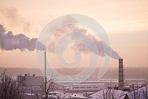 Smoke from two industrial chimneys pipes on the pink sunrise background in winter.