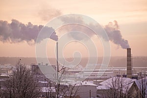 Smoke from two industrial chimneys pipes on the pink sunrise background in winter.