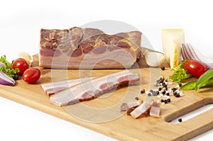 Smoked bacon slab on cutting board sliced with vegetables