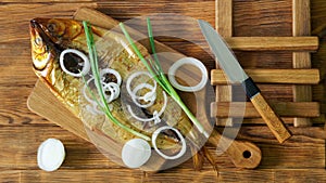 Smoked Baikal omul, green and onions on a cutting board on a wooden rustic table made of pine boards next to a knife. A rare fish