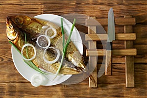 Smoked Baikal omul Ð°nd onion in a white plate on a wooden table made of pine boards next to a knife. Rare fish delicacy - omul.