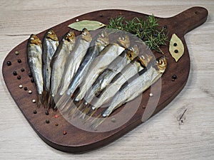Smoked Baltic herring with spices, juniper sprig on a wooden kitchen board, light background, top view, flat layout.