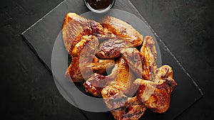 Smoked chicken wings on a slate board, top view, rotation.