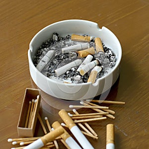 Smoked cigarettes in white ashtray and matchstick