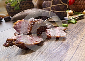 Smoked dried gammon ham and slices of sausages with bread, tomatos, herbs, garlic and basketson wooden board