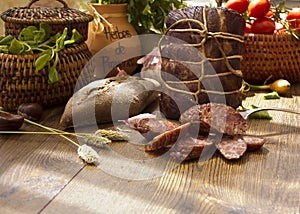 Smoked dried gammon ham and slices of sausages with bread, tomatos, herbs, garlic and basketson wooden board