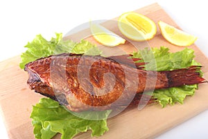 Smoked fish and lemon on green lettuce leaves on Wooden cutting board isolated on white background.