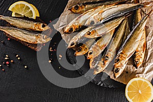 Smoked fishes sprat marinated with spices, salt, greens and slice of bread on plate over dark stone background. Mediterranean food