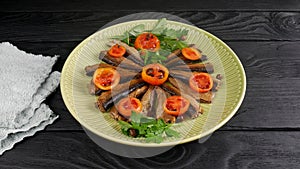 Smoked fishes of sprats without their heads with sliced tomatoes, parsley and spices in a  plate on a  table