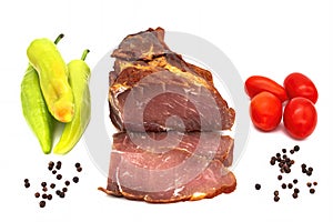 Smoked ham cut into slices with different vegetables isolated on a white background
