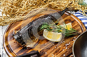 Smoked mackerel fish with lemon and rosemary on cutting board over wooden rustic background. Seafood, healthy food, close up