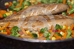Smoked mackerel with vegetables cooked in a frying pan.