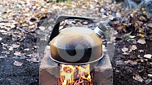 Smoked metal kettle boils on fire on bricks outdoors