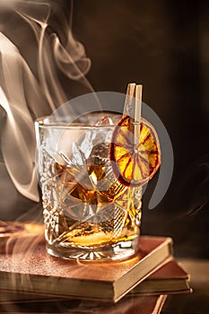 Smoked old fashioned rum cocktail with cubes of ice around on a dark background