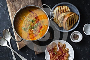 Smoked paprika lentil soup with grilled cheese sandwiches and crispy bacon on a dark background, top view. Delicious comfort food