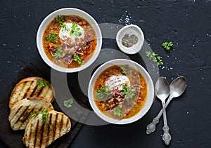 Smoked paprika lentil soup in the pan with grilled cheese sandwiches and crispy bacon on a dark background, top view. Delicious co