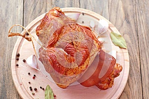 Smoked pork meat knuckle with garlic, pepper and laurel bay on wooden background