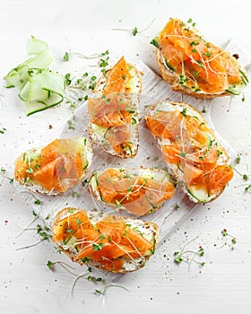 Smoked salmon bruschettas with soft cheese and cucumber shavings on white board.