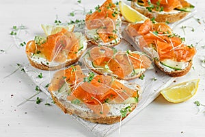 Smoked salmon bruschettas with soft cheese and cucumber shavings on white board.