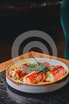 Smoked salmon rolls with cream cheese served in a white on a black table with blurred background.