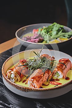 Smoked salmon rolls with cream cheese served in a white on a black table with blurred background.