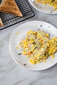 Smoked salmon with scrambled eggs, whole grain bread toast and dill on marble background