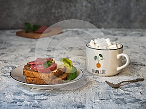 Smoked sausage and cheese sandwiches on toasted bread, tomato wedges and coffee in a white mug