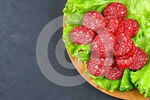 Smoked sausage, salami chopped in slices on a salad on a wooden circular cutting board on a concrete gray table.