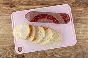 Smoked sausage and slices of bread on cutting board on wooden table. Top view