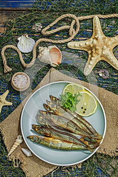 Smoked smelt with fresh lemon and herbs. Salted fish with marine decor. Trendy dish, sea rope