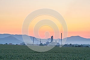 Smokestack of a concrete factory in grain field and mountains at background. Czech Republic. Europe.