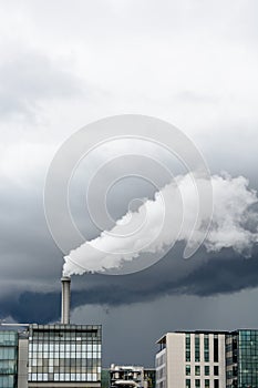 A smokestack emitting white fumes against a stormy sky