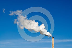 Smokestack and horizontal white smoke on blue sky.