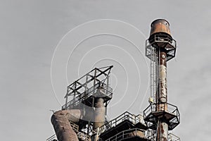 Smokestack with ladders and catwalks against a grey sky, steel mill