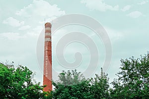 Smokestack in shape of wine bottle neck with text In vino veritas. Industrial chimney on cloud sky background and tree crowns.