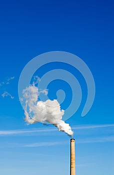 Smokestack and vertical white smoke on blue sky.