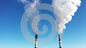 Smokestack with white smoke smoking into the sky close-up aerial view.