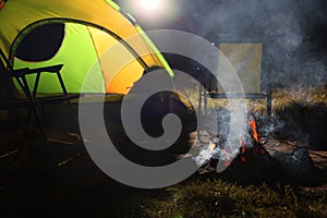 Smoking bonfire and folding chairs near camping tent outdoors in evening