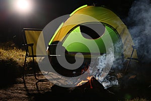 Smoking bonfire and folding chairs near camping tent outdoors at night