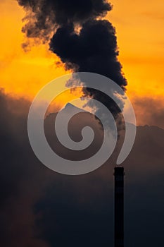 Smoking chimney and mountains with colorful sky at background