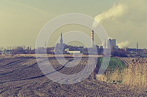 Smoking chimney stack of a power station near a farm field