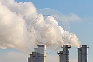 Smoking chimneys on background of the blue sky as an illustration of the pollution of nature and a disbalance of the ecology
