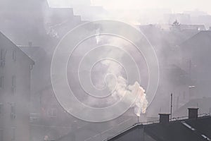 Smoking chimneys at roofs of houses emits smoke, smog at sunrise, pollutants enter atmosphere. Environmental disaster.