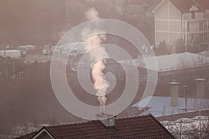 Smoking chimneys at roofs of houses emits smoke, smog at sunrise, pollutants enter atmosphere. Environmental disaster.
