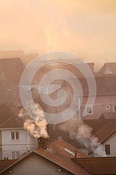 Smoking chimneys at roofs of houses emits smoke, smog at sunrise, pollutants enter atmosphere. Environmental disaster.