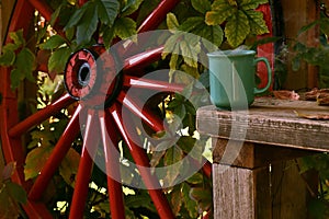 A smoking hot coffee mug on a wooden bench, with an old wooden wagon wheel