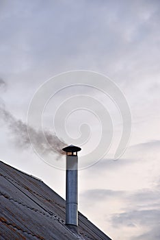 The smoking iron chimney of an old house in the evening