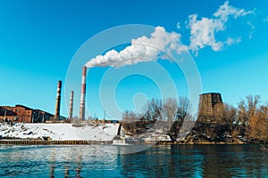 Smoking pipes of the plant against the blue sky, white smoke from the pipes