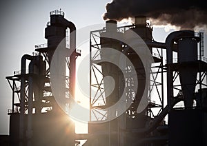 Smoky chimneys silhouettes against sun.